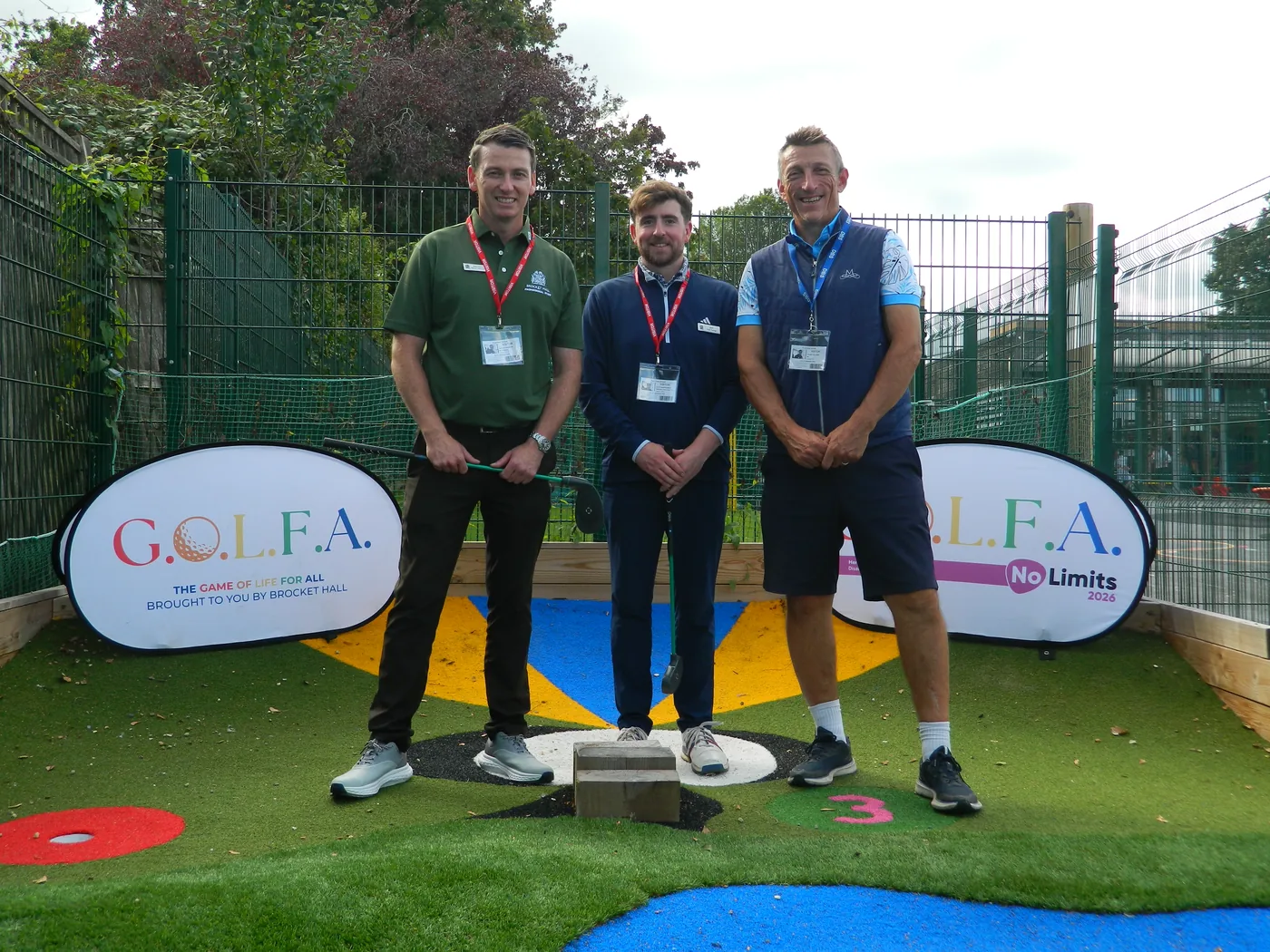 Three men from Brocket Hall wearing visitor lanyards standing on the adventure golf course between two GOLFA banners